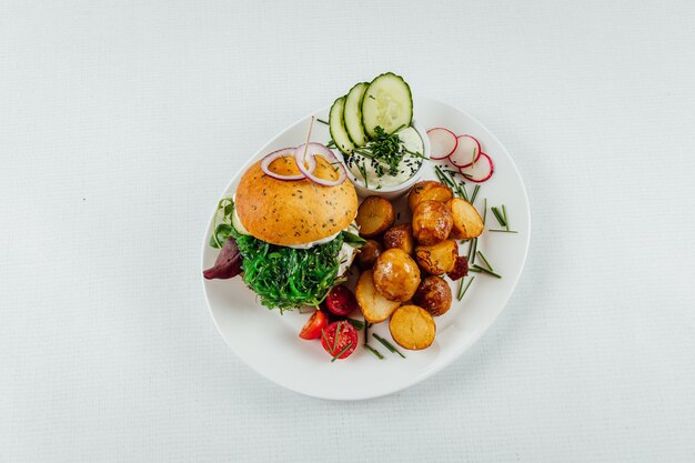 Top view closeup of roasted potatoes with tomato and radish next to a burger with arugula