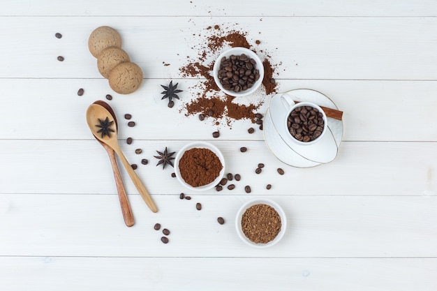 Free photo top view coffee beans in cup and bowl with grinded coffee, spices, cookies, wooden spoons on wooden background. horizontal