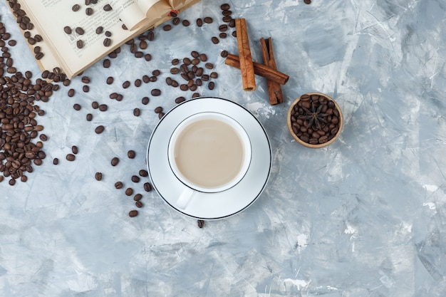 Top view coffee in cup with coffee beans, book, cinnamon sticks on grey plaster background. horizontal