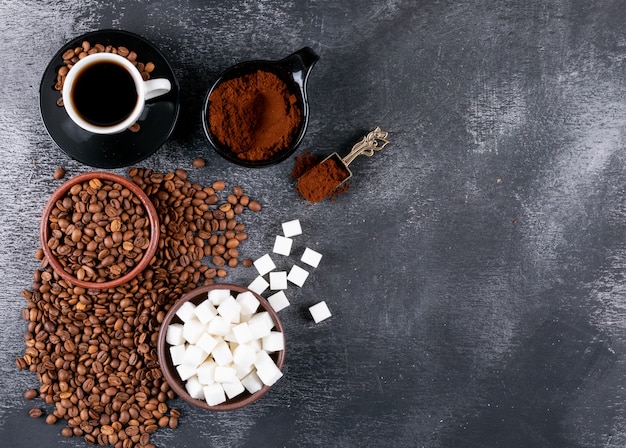 Top view coffee cup with coffee beans and sugar cubes on dark table