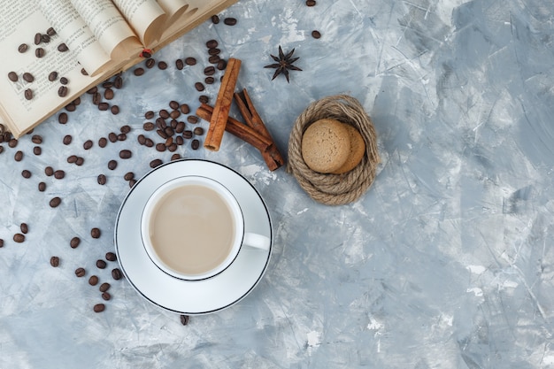 Top view coffee in cup with cookies, coffee beans, book, spices on grey plaster background. horizontal