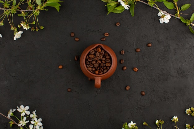 top view coffee seeds brown whole inside brown pot around white flowers on the dark