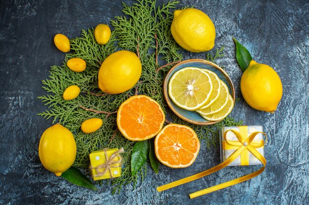 Top view of collection of half and whole citrus fruits on fir branches a gift box on dark background