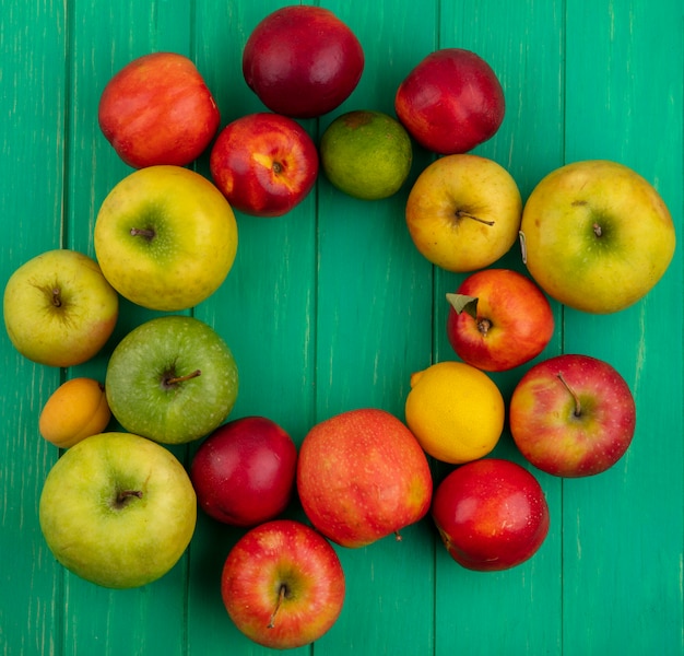 Free photo top view of colored apples with peaches lemon and lime on a green surface