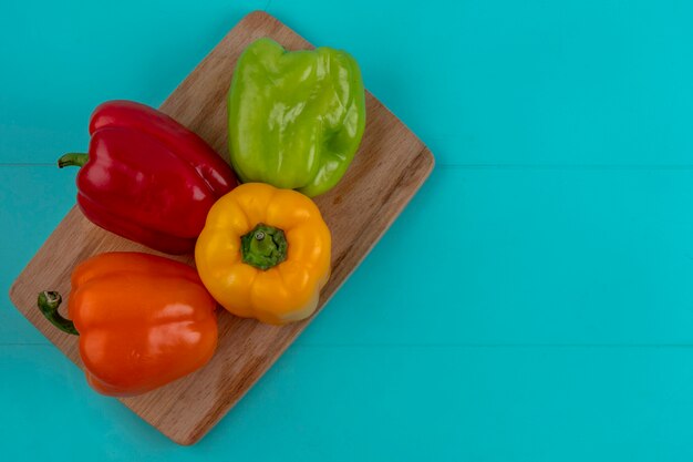 Top view of colored bell peppers on a cutting board on a turquoise surface