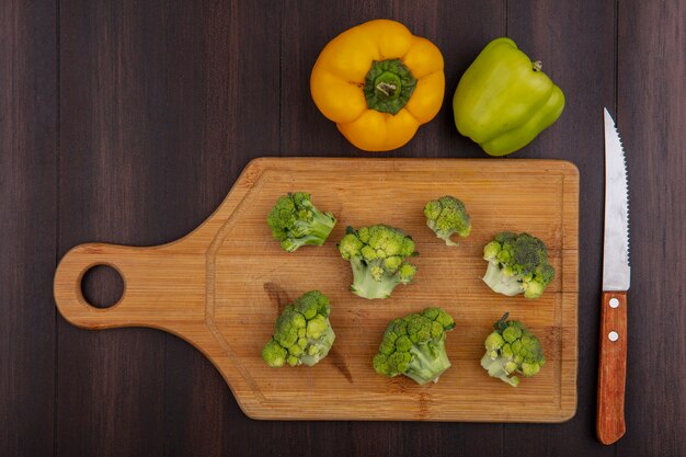 Top view colored bell peppers with broccoli on cutting board with knife  on wooden background