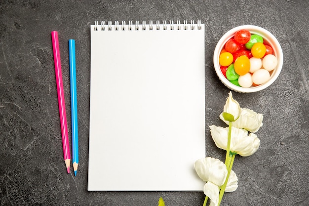 Top view colorful candies with notepad and pencils on grey space