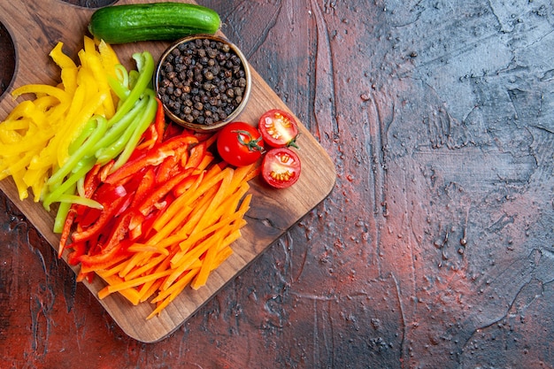 Top view colorful cut peppers black pepper tomatoes cucumber on chopping board on dark red table with copy space