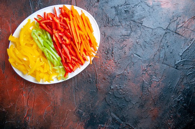 Top view colorful cut peppers on white plate on dark red table with free place