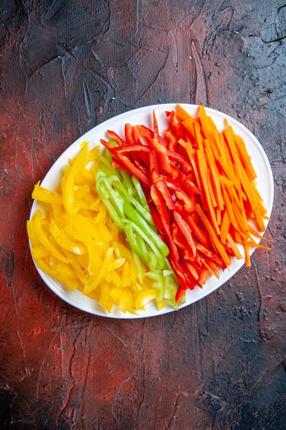 Top view colorful cut peppers on white plate on dark red table