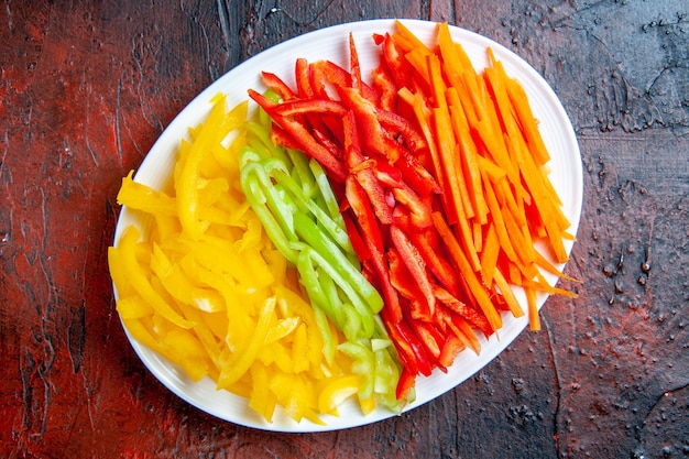 Top view colorful cut peppers on white plate on dark red table