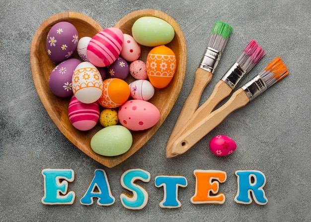 Top view of colorful easter eggs in heart shaped plate with paint brushes