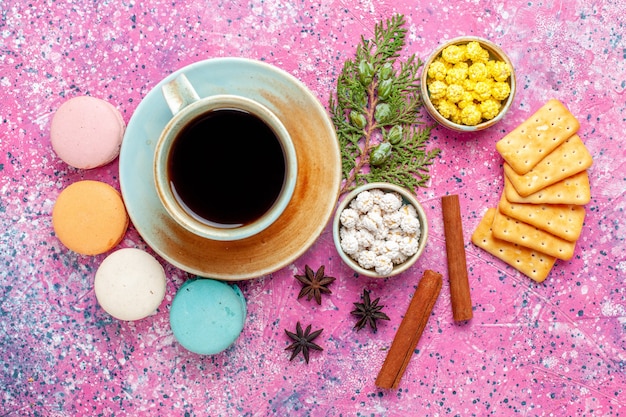 Top view colorful french macarons with cinnamon crackers and cup of tea on pink desk bake cake sweet sugar pie color