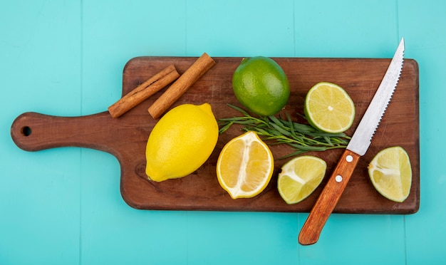 Top view of colorful lemons on wooden kitchen board with knife and cinnamon sticks on blue