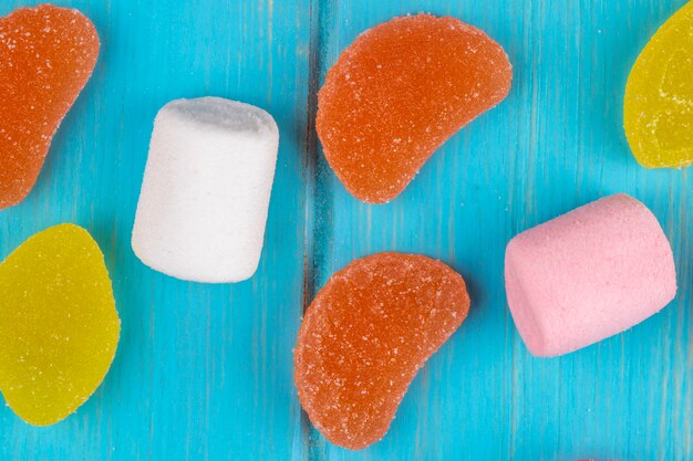 Top view of colorful tasty marmalade candies and marshmallows scattered on blue