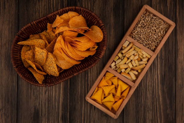 Top view of cone shape bugles chips on a wooden divided plate with shelled sunflower seeds with spicy chips on a bucket on a wooden wall