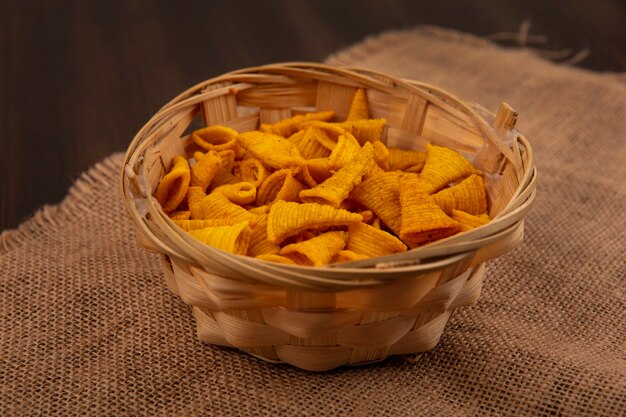 Top view of cone shape fried corn snacks on a bucket on a sack cloth on a wooden table