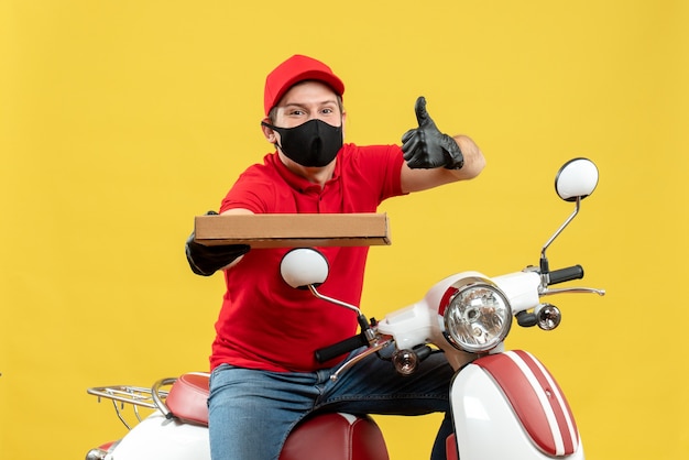 Top view of confident happy courier man wearing red blouse and hat gloves in medical mask sitting on scooter showing order with thumbs up