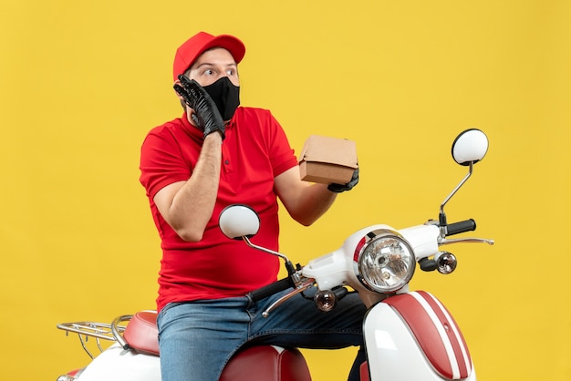 Top view of confused delivery guy wearing uniform and hat gloves in medical mask sitting on scooter showing order