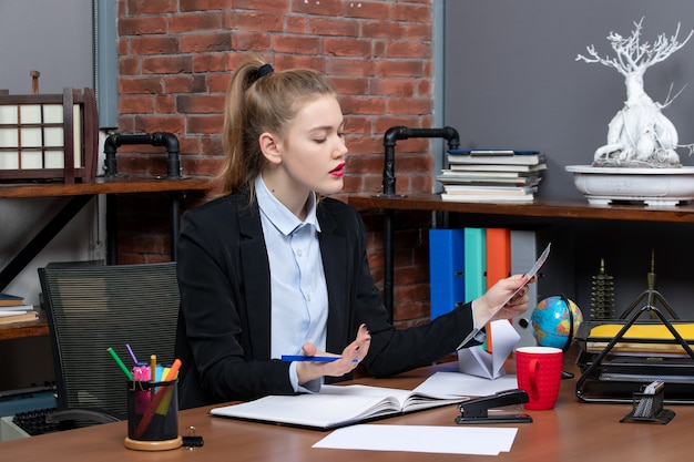 Top view of confused young woman sitting at a table and reading a document in the office