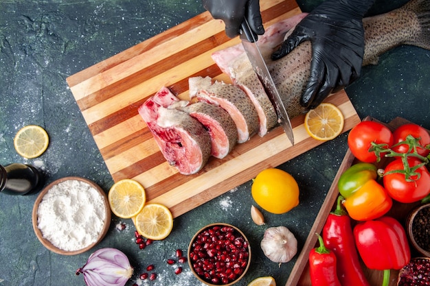 Free photo top view cook cutting raw fish on cutting board vegetables on wood board lemon on table