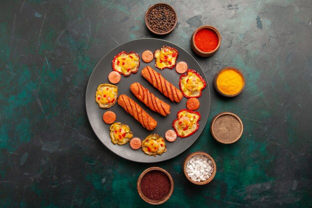 Top view cooked bell-peppers with sausages and seasonings on dark-green surface