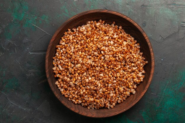 Top view cooked buckwheat tasty meal inside brown plate on dark-green surface