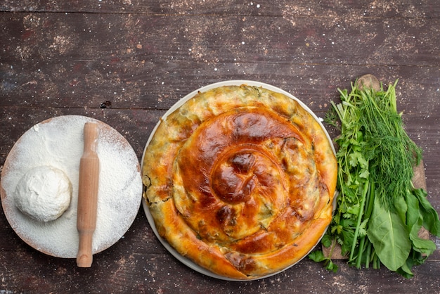 Free Photo top view cooked greens pastry along with greens and dough on the brown wooden desk food meal bread photo