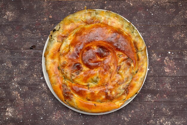 Top view cooked greens pastry inside round plate on the brown wooden desk food meal pastry green