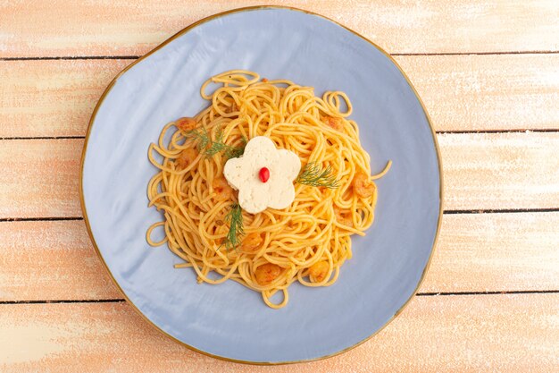 Top view of cooked italian pasta tasty meal with greens inside blue plate on the cream wooden rustic surface