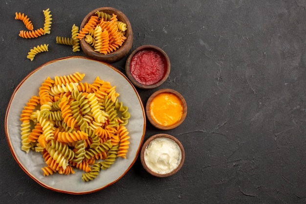 Top view cooked italian pasta unusual spiral pasta with seasonings on dark space