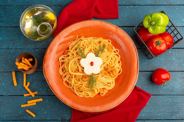 Top view of cooked italian pasta with greens inside orange plate with oil and vegetables on the blue wooden surface