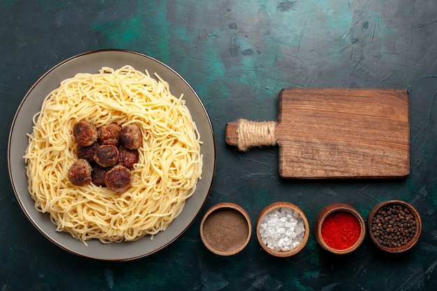 Top view cooked italian pasta with meatballs and seasonings on dark-blue desk