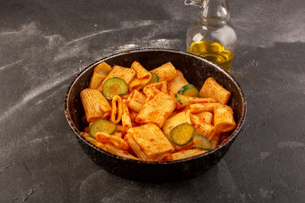 A top view cooked italian pasta with tomato sauce and cucumber inside pan on the dark table food meal italian pasta dish