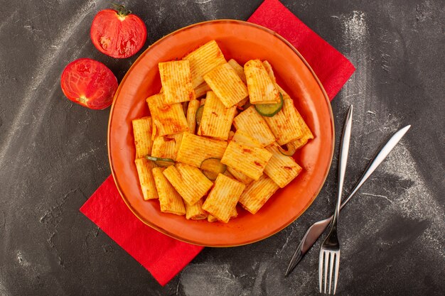 A top view cooked italian pasta with tomato sauce and cucumber inside plate