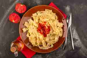 Free photo a top view cooked italian pasta with tomato sauce inside plate with cutlery and tomatoes