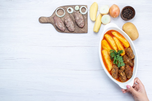 Free photo top view of cooked meat cutlets with sauce potatoes and greens along with raw meat on light desk, food meal meat vegetable