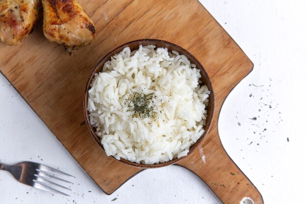 Top view of cooked rice tasty meal inside brown pot with oil and chicken on white surface