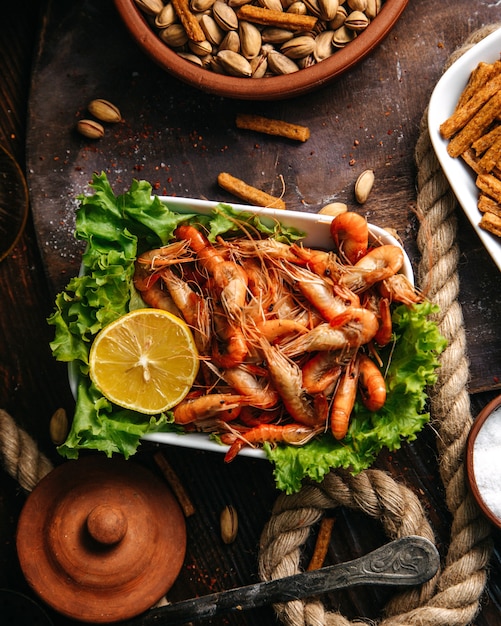 A top view cooked shrimps with green salad and lemon on the wooden table food meal seafood