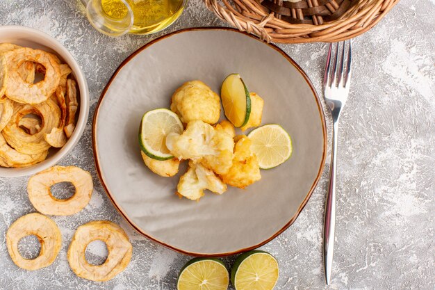 Top view of cooked sliced cauliflower inside plate with lemon and oil on the light white surface