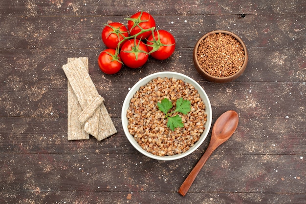 Top view cooked tasty buckwheat inside plate with crisps and red tomatoes on dark