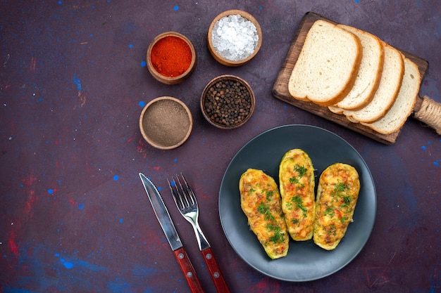 Top view cooked tasty squashes with seasonings and bread loafs on dark-purple desk.