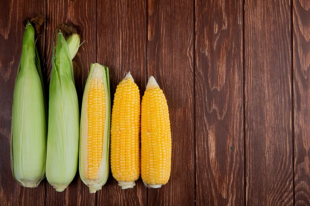 Top view of cooked and uncooked corn cobs on left side and wooden surface with copy space