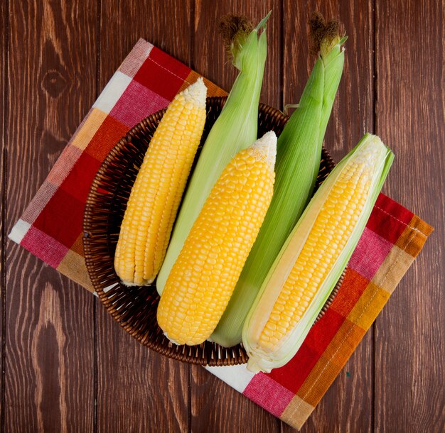 Top view of cooked and uncooked corns in basket on cloth and wood