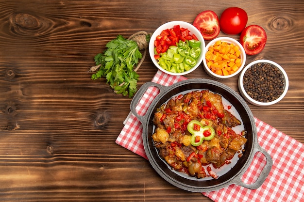 Top view cooked vegetable meal including vegetables sauce and meat on brown desk