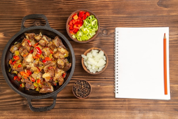 Top view cooked vegetable meal with meat and fresh sliced bell-pepper on the wooden brown desk