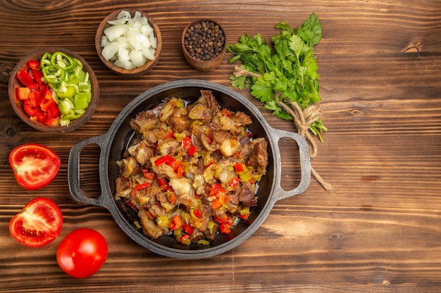 Top view cooked vegetable meal with meat and fresh sliced bell-pepper on the wooden brown desk