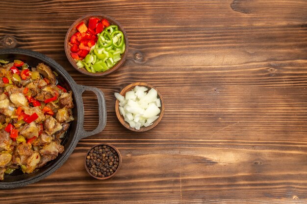 Top view cooked vegetable meal with meat and fresh sliced bell-pepper on wooden brown desk