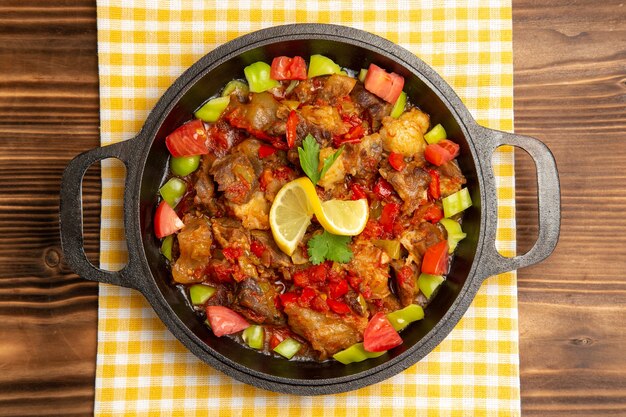 Top view cooked vegetable meal with meat and sliced bell-peppers inside pan on the brown desk