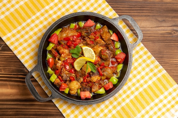 Top view cooked vegetable meal with meat and sliced bell-peppers inside pan on the brown wooden desk